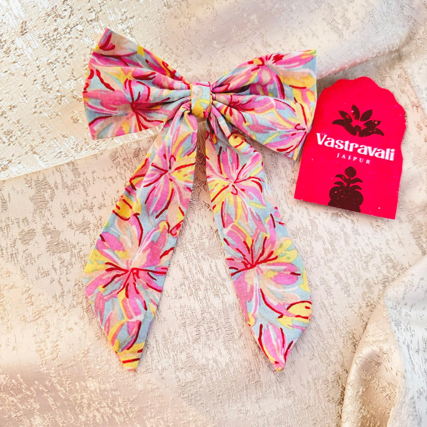 A pink floral hair bow with a branded tag in the background.