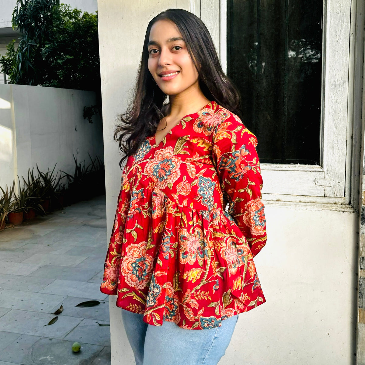 A woman wearing a red floral top with a round neckline and 3/4 sleeves, standing outdoors.