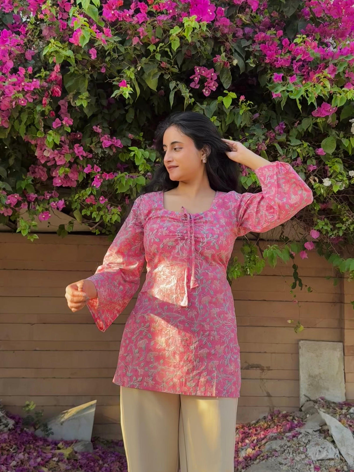 Woman in a pink floral top standing in front of a flowering bush