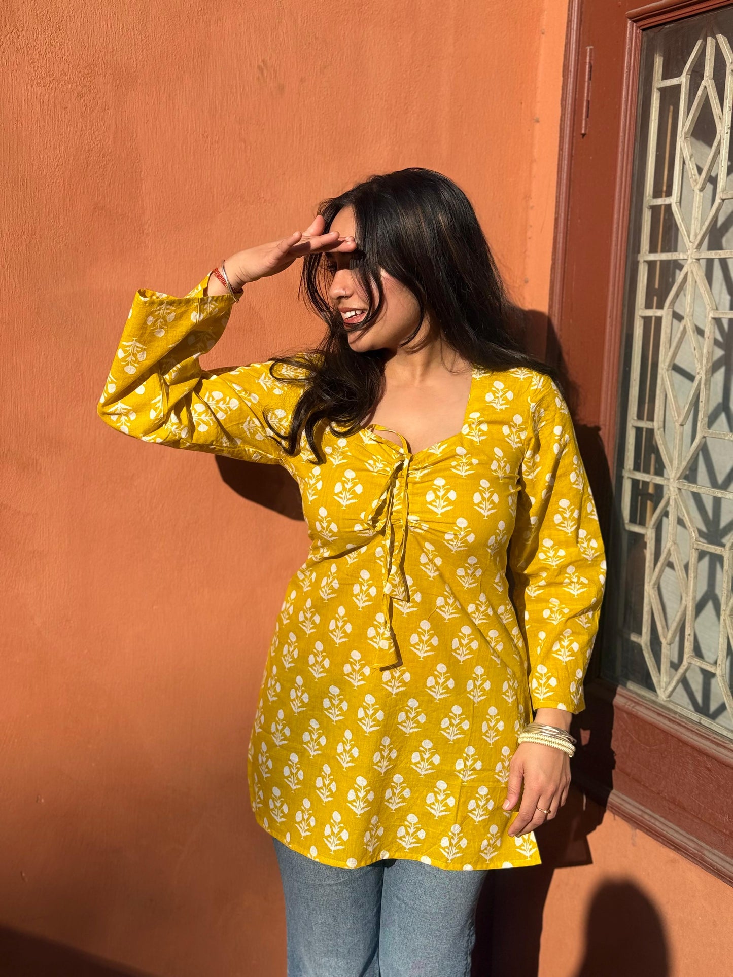 Woman wearing a yellow floral blouse against an orange wall.