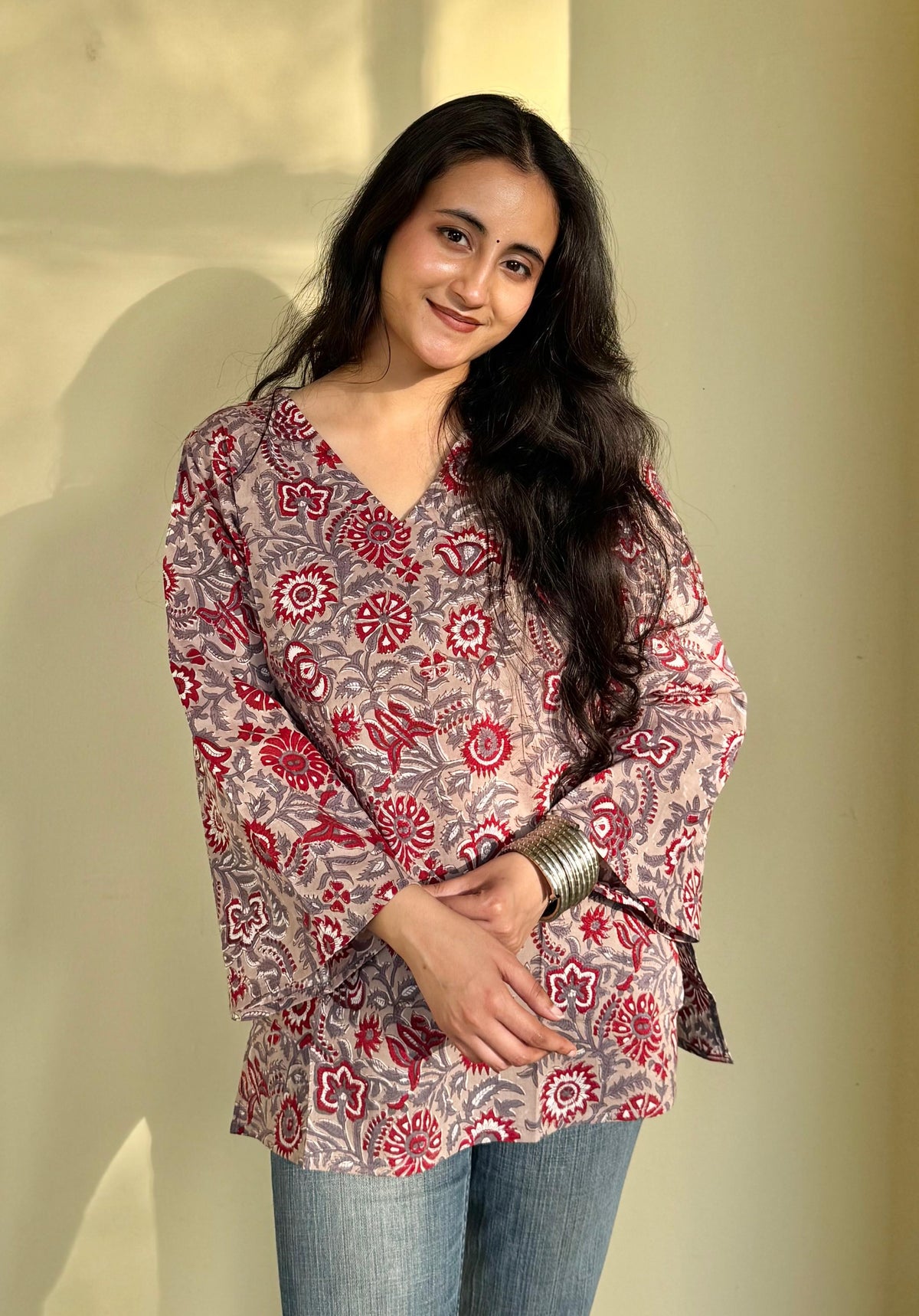 A woman wearing a red and beige hand-block printed short kurti with flared sleeves, paired with blue jeans.
