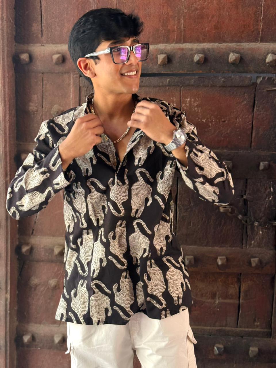 Man wearing a patterned shirt and sunglasses in front of a textured wall.