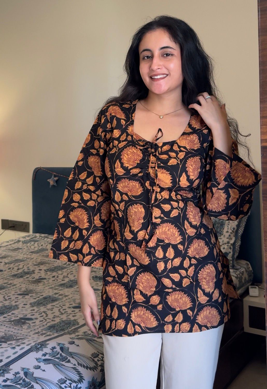 Woman wearing a black and orange floral patterned top indoors.