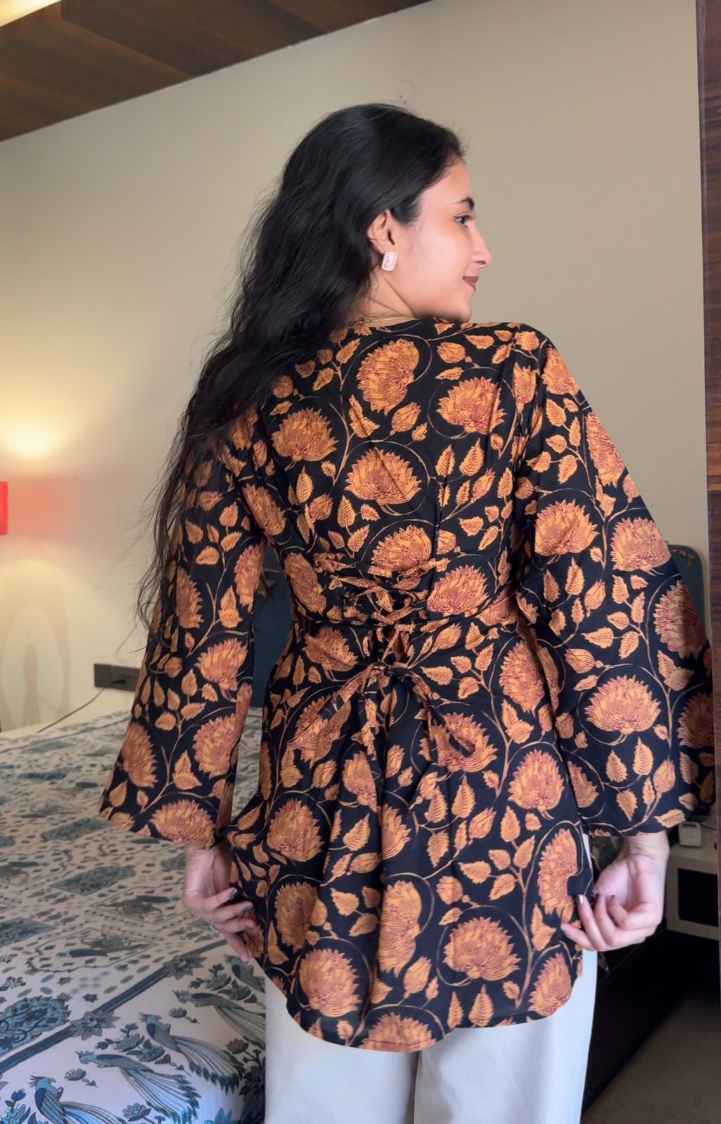 Woman wearing a black and orange patterned kimono-style garment in a room.