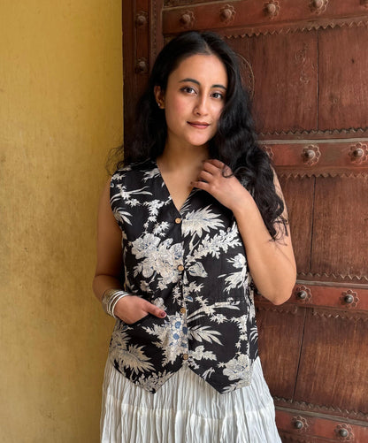 A woman wearing a black and white floral vest top with a round neckline and two pockets, paired with a white skirt.