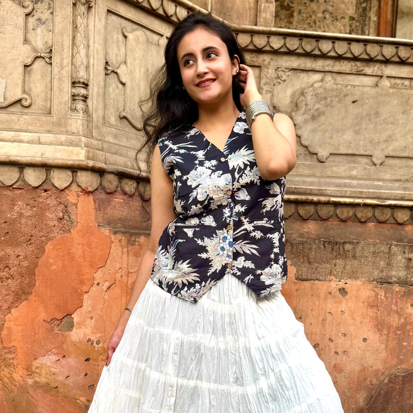 A woman wearing a black and white floral vest top with sleeve details, paired with a white skirt.