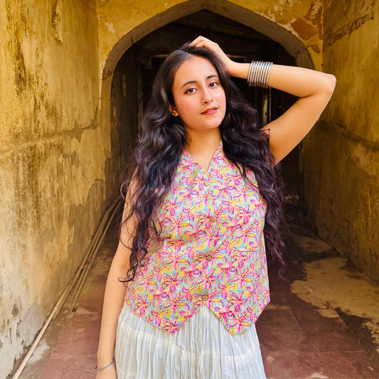 A woman wearing a pink and multicolor floral vest top with two pockets, posing in a historic building with an arched doorway.