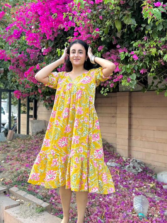 Woman in a yellow floral dress standing in front of pink flowers