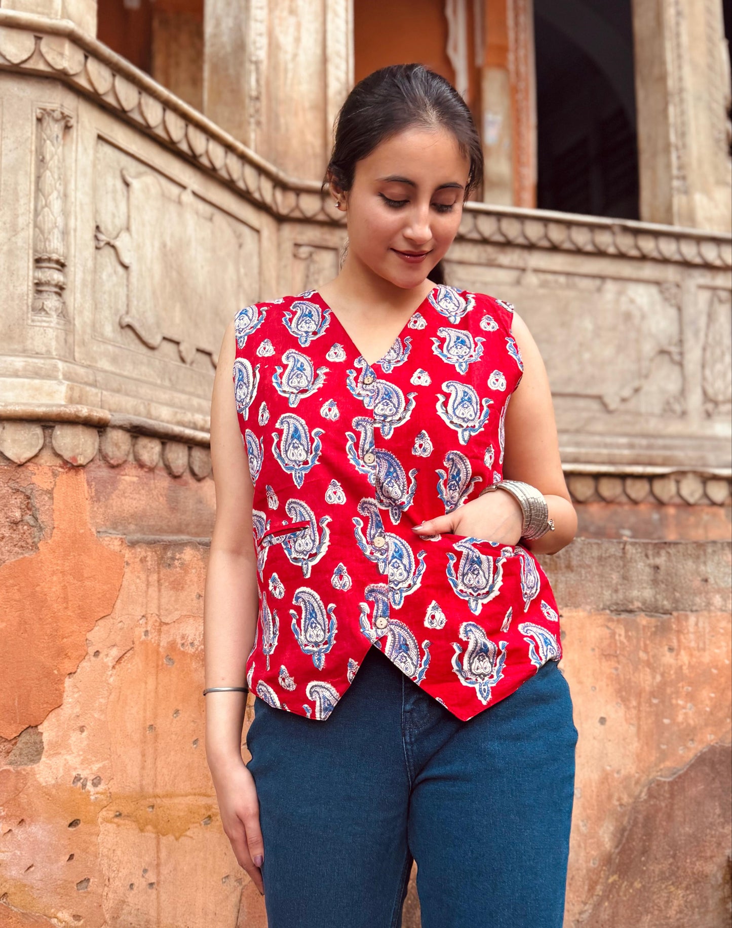 A woman wearing a red and blue geometric patterned vest top with a round neckline, paired with blue jeans.