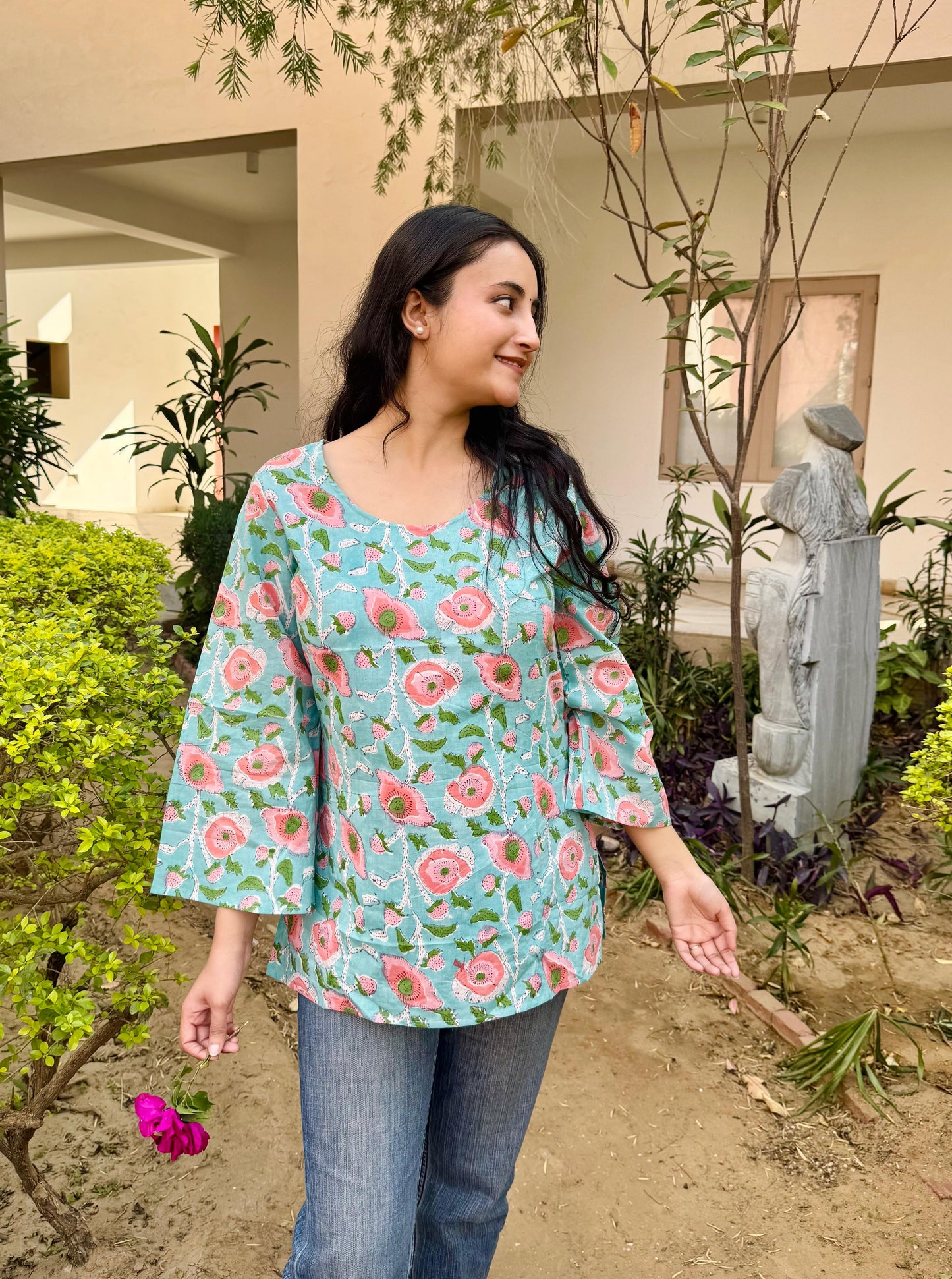 A woman wearing a short kurti with hand-block print design in blue, pink, and green colors.