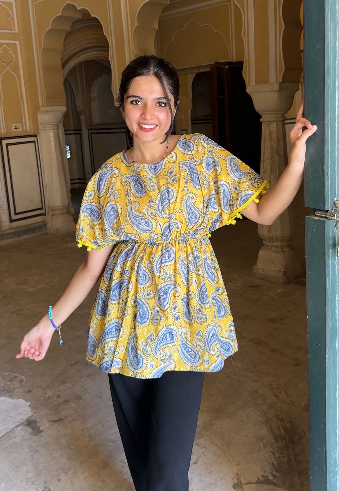 Woman wearing a yellow and blue patterned blouse in an indoor setting with arches.