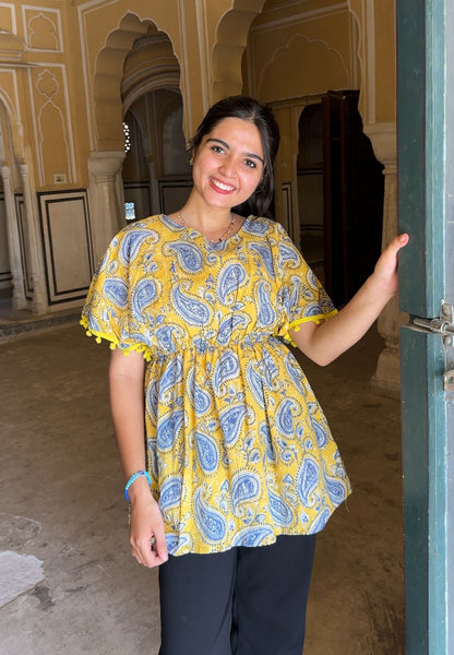 Woman wearing a yellow and blue patterned blouse standing in an ornate indoor setting.