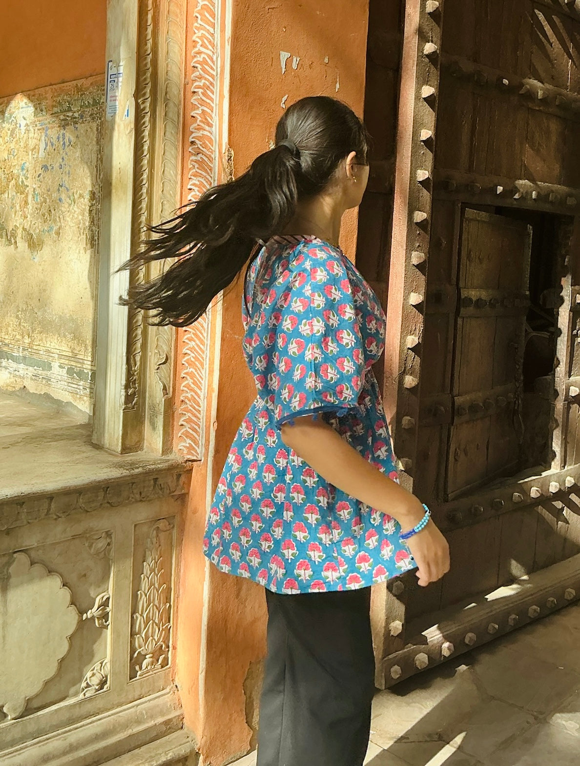 Woman in a blue floral shirt standing in front of an ornate wooden door.
