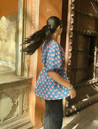 Woman in a blue floral shirt standing in front of an ornate wooden door.
