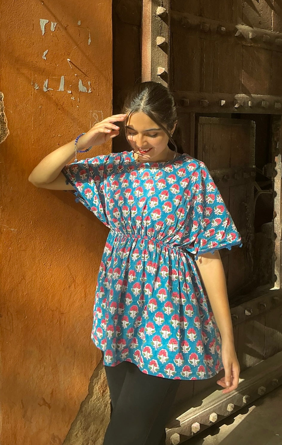 Woman wearing a blue patterned dress standing against a wooden wall.