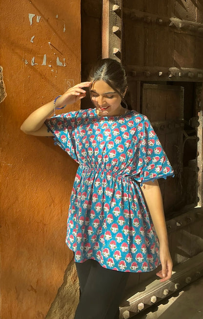 Woman wearing a blue patterned dress standing against a wooden wall.