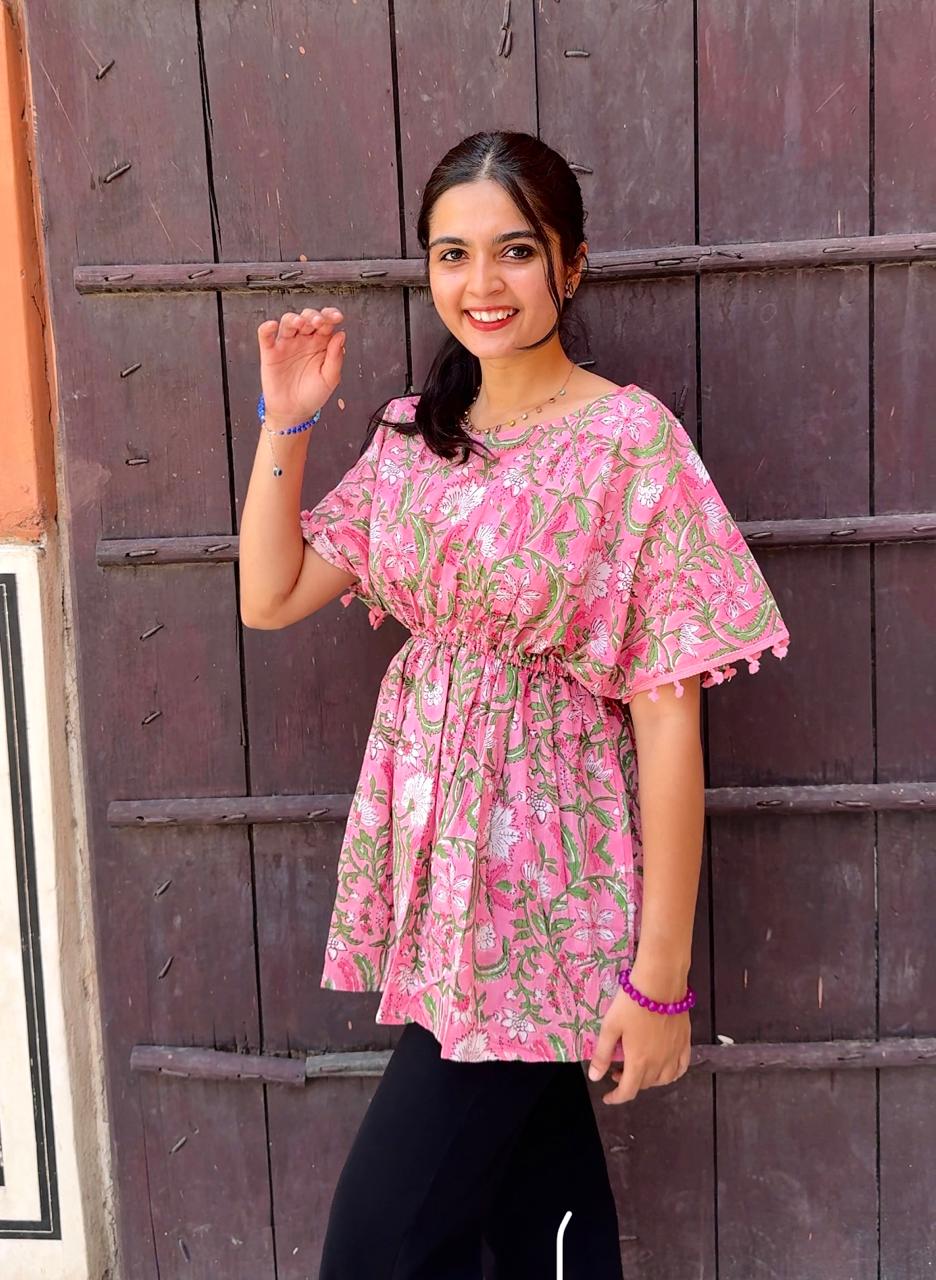 Woman wearing a pink floral dress standing in front of a wooden door.
