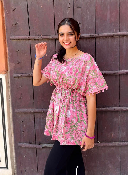 Woman wearing a pink floral dress standing in front of a wooden door.
