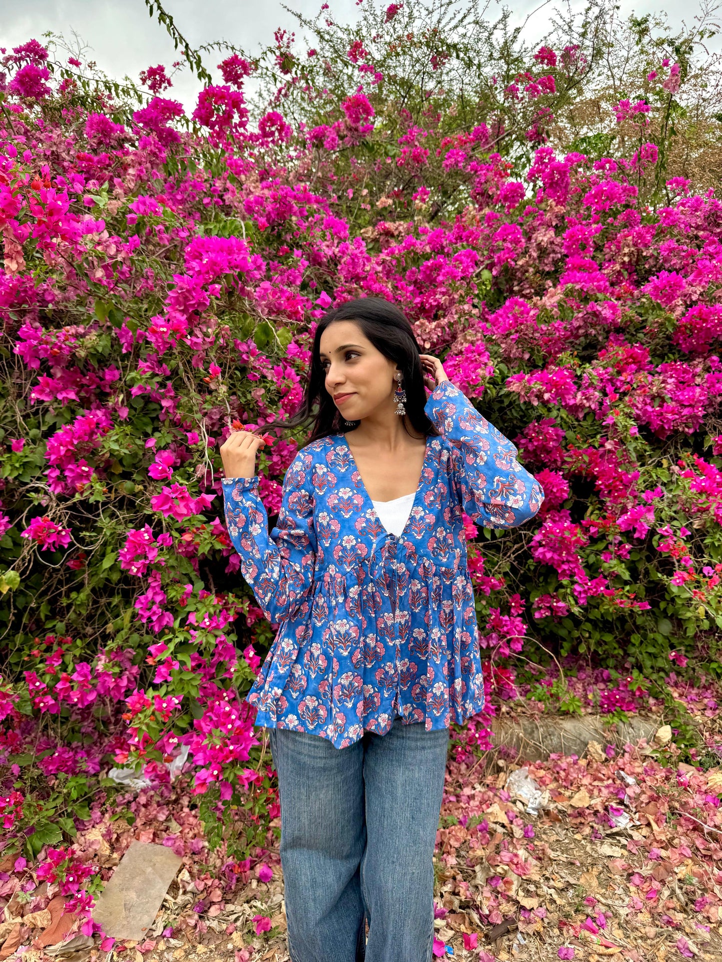 Woman in a blue floral blouse standing in front of pink flowers