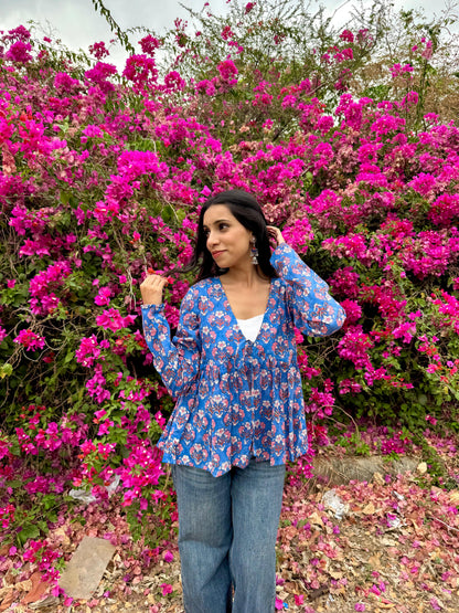 Woman in a blue floral blouse standing in front of pink flowers