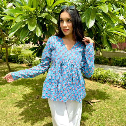 A woman standing in a garden wearing a blue and white floral kurti with 3/4 length sleeves and a V-neck.