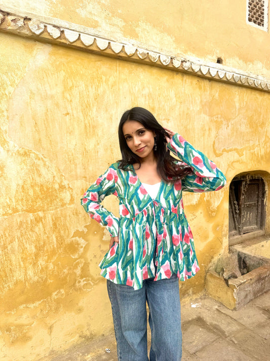 Woman in a colorful top and jeans standing against a yellow wall.