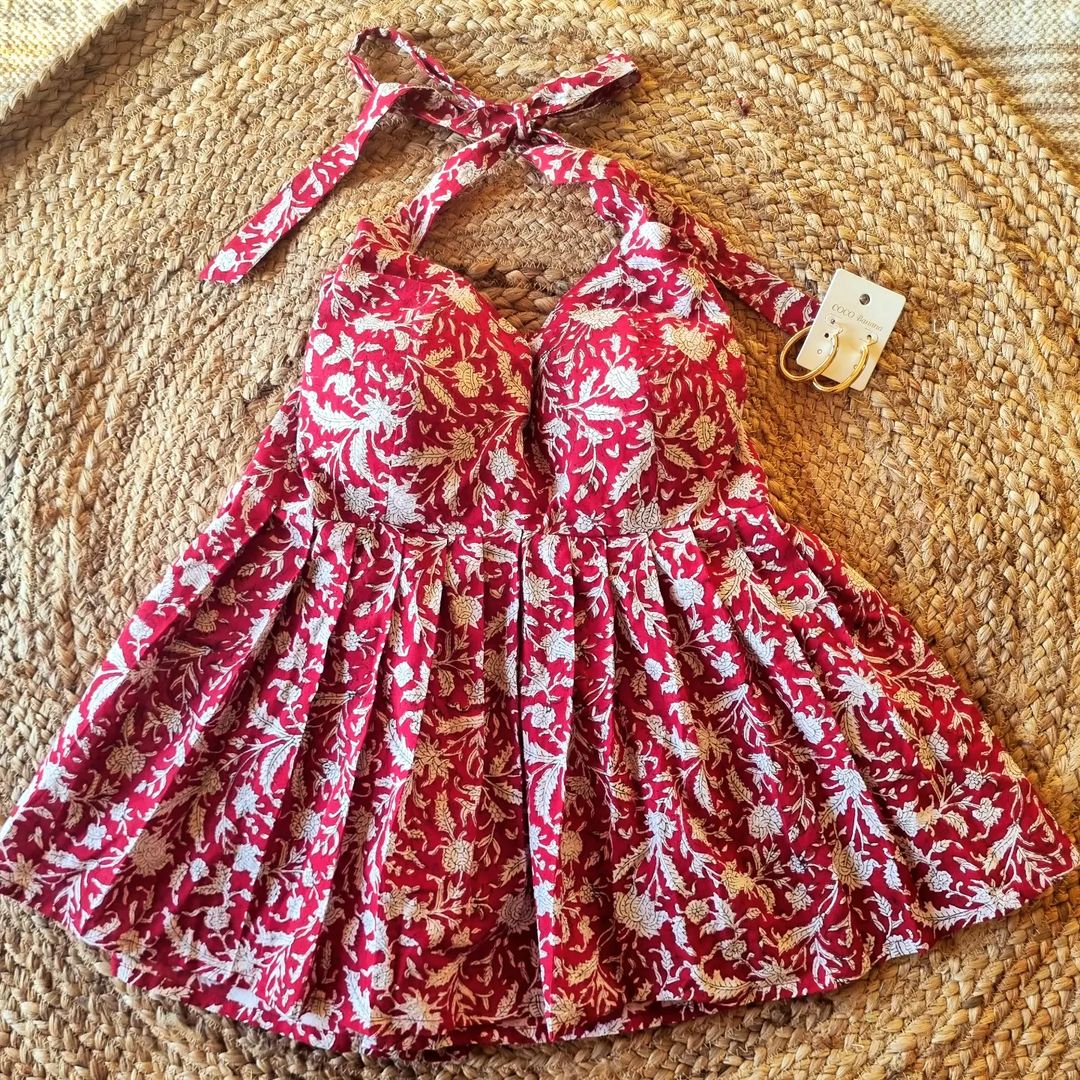 A red halter neck top with a floral pattern, displayed on a woven surface.