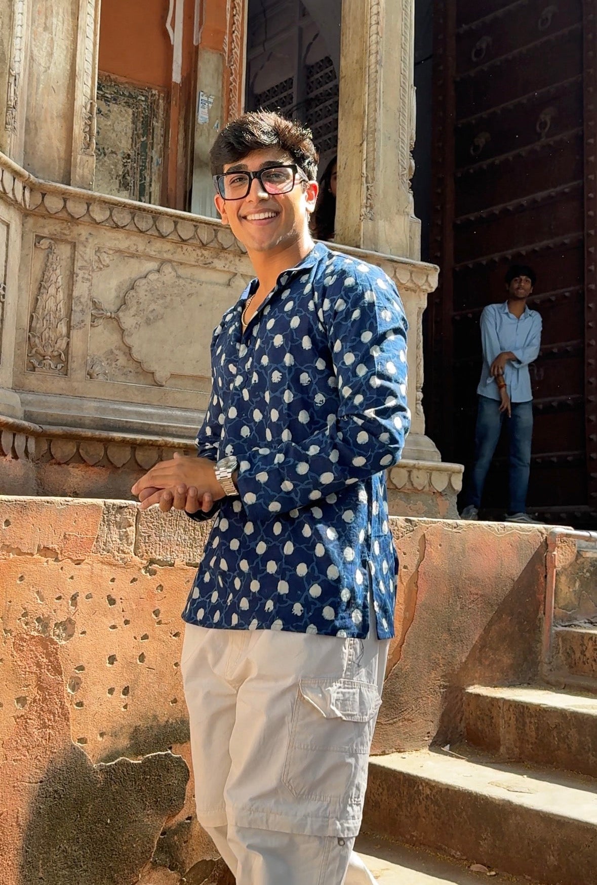 Man in a blue patterned shirt standing in front of an architectural structure