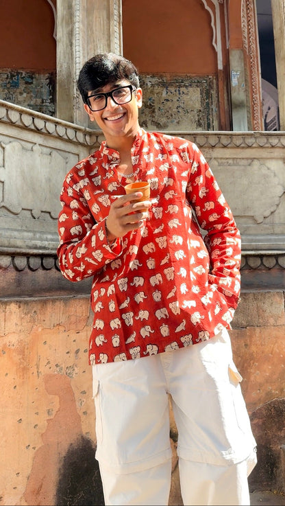 Person wearing a red patterned shirt and white pants standing in front of ornate architecture.