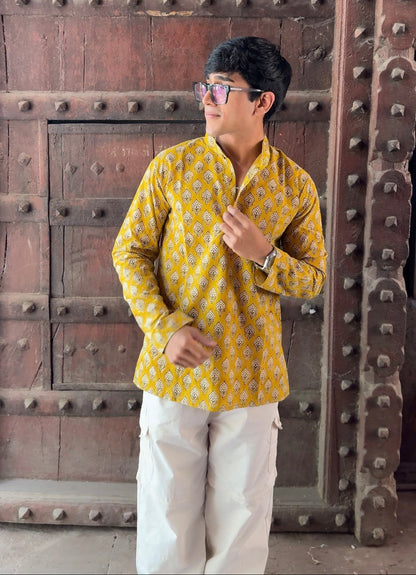 Person wearing a yellow patterned shirt and white pants standing in front of a large wooden door.