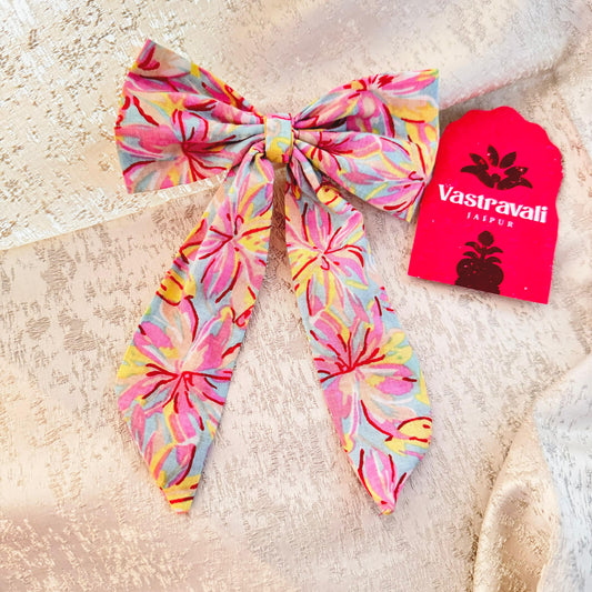 A pink floral hair bow with a branded tag in the background.