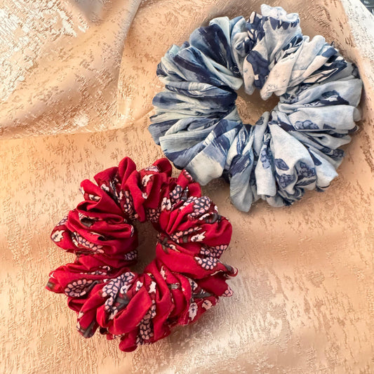 Two fluffy scrunchies on a textured background, one with a red pattern and the other with a blue and white pattern.