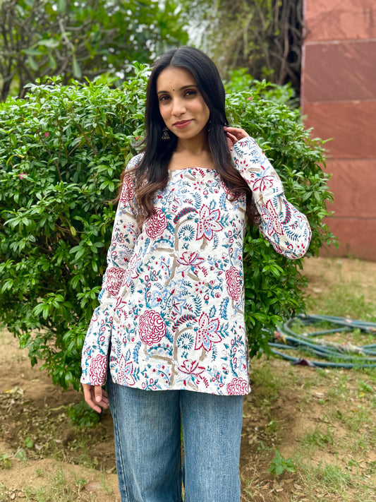 Woman wearing a floral blouse standing outdoors with greenery in the background