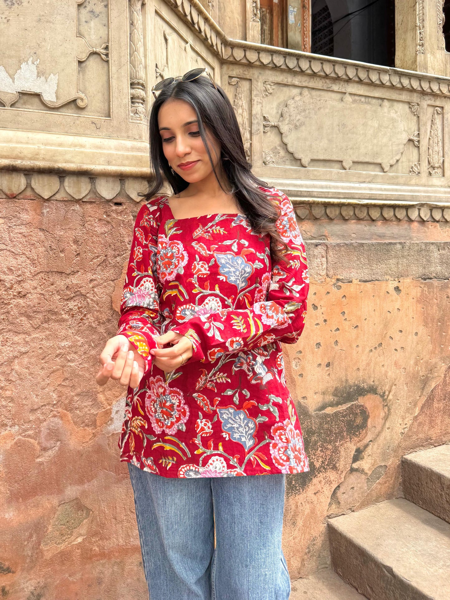 Woman wearing a red floral blouse standing in front of an ornate stone wall.