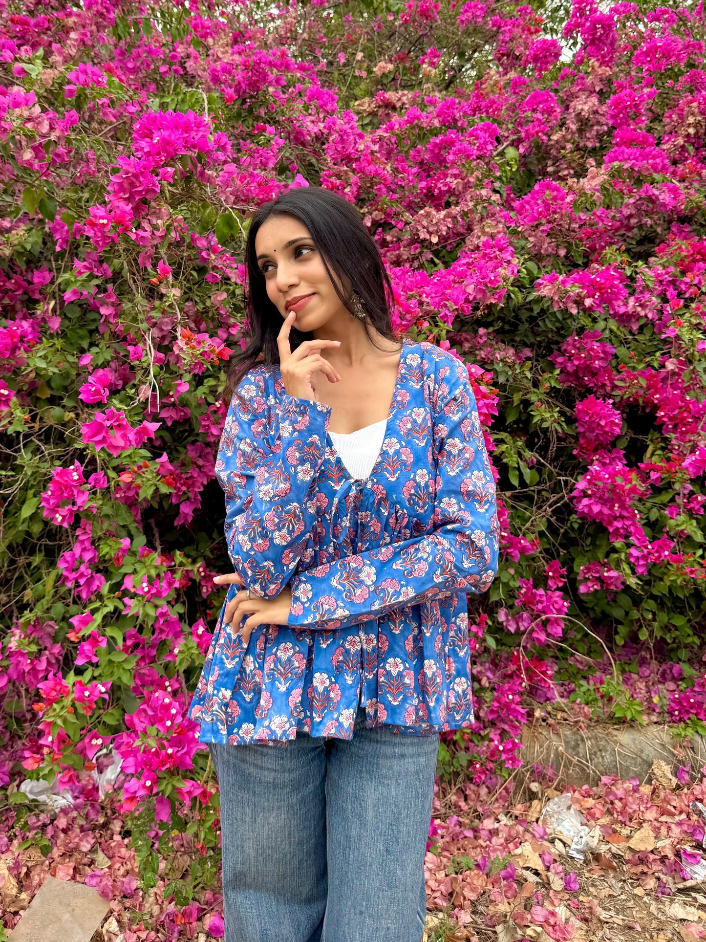 Woman in a blue floral blouse standing in front of a vibrant pink flowering bush.