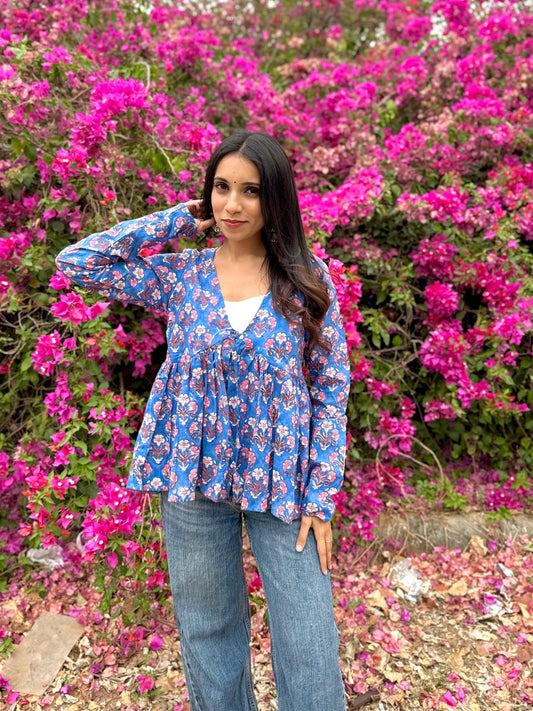 Woman in a blue floral blouse standing in front of pink flowers