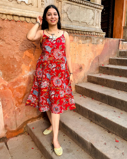 A woman standing on a set of stairs, wearing a red hand-block printed floral dress with three-quarter length sleeves and open-toe heels.