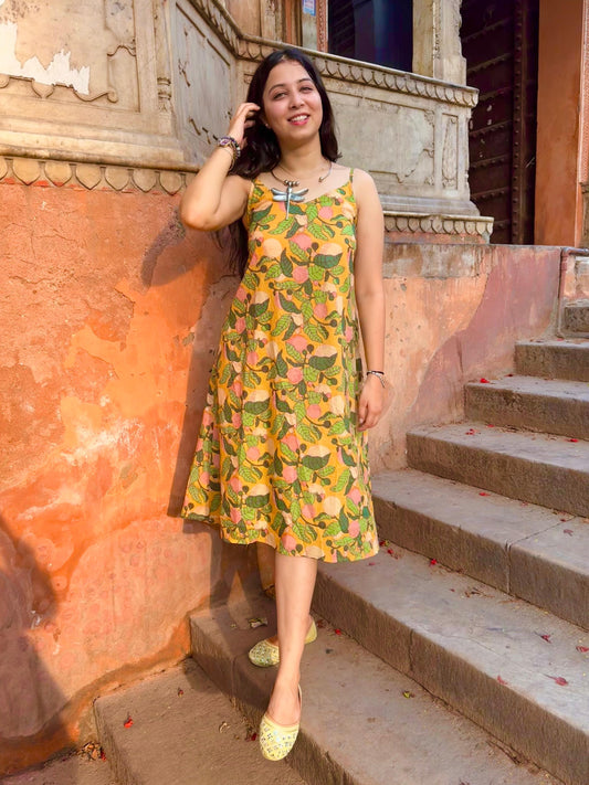 A woman standing on a set of stairs, wearing a vibrant yellow and green floral dress with 3/4 length sleeves and a V-neckline, posing with one hand on her hip.