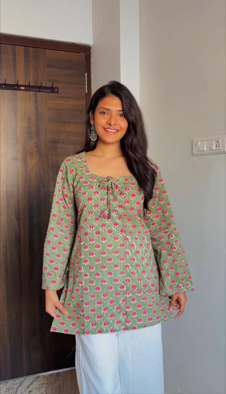 Woman wearing a green floral patterned top in a room with a wooden wardrobe.