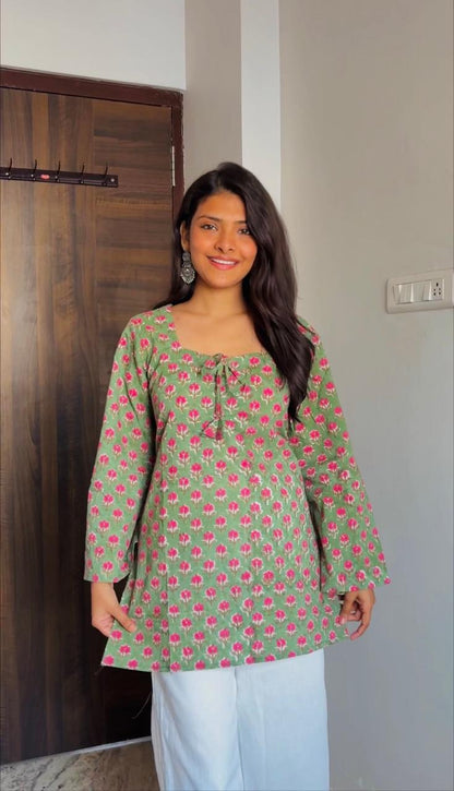 Woman wearing a green floral patterned top in a room with a wooden wardrobe.