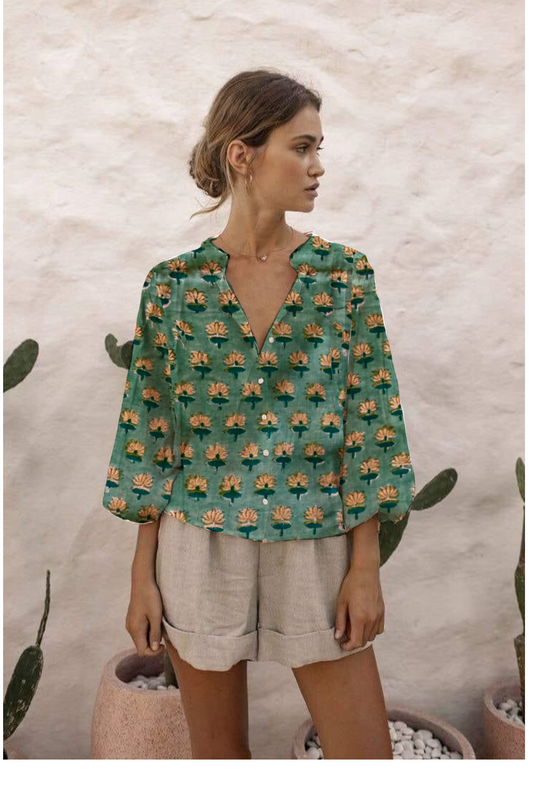 Woman wearing a green patterned blouse with beige shorts against a textured wall.