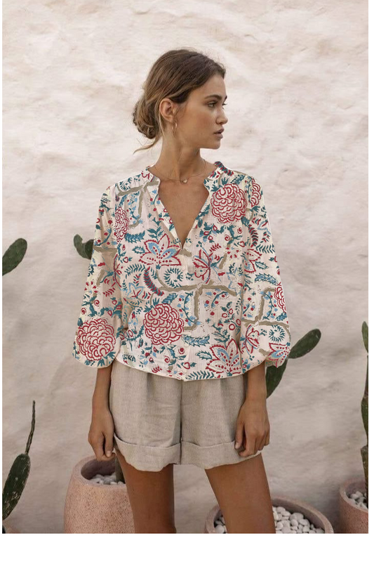 Woman wearing a floral blouse and beige shorts against a textured wall.