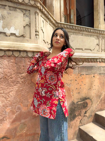 Woman in a red floral blouse standing against an ornate wall.