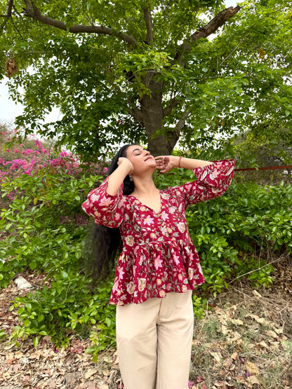Woman in a red floral blouse standing outdoors with greenery and flowers in the background