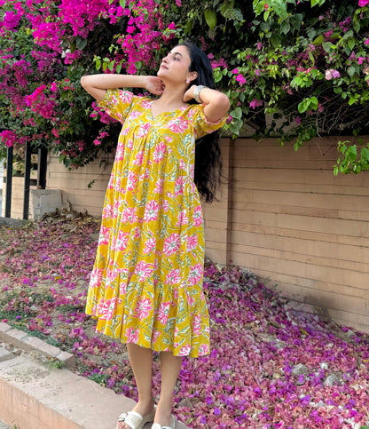 Woman in a yellow floral dress standing in front of pink flowers
