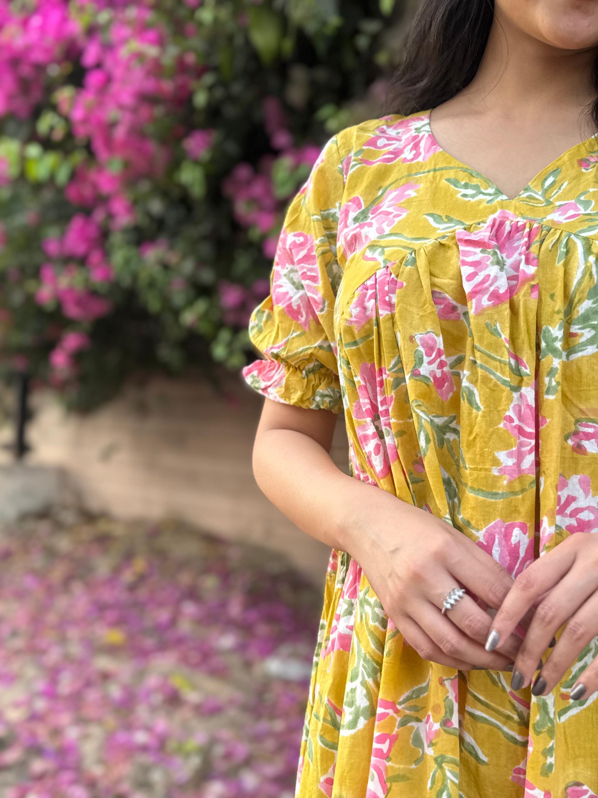 Person wearing a yellow floral dress with pink flowers in an outdoor setting.