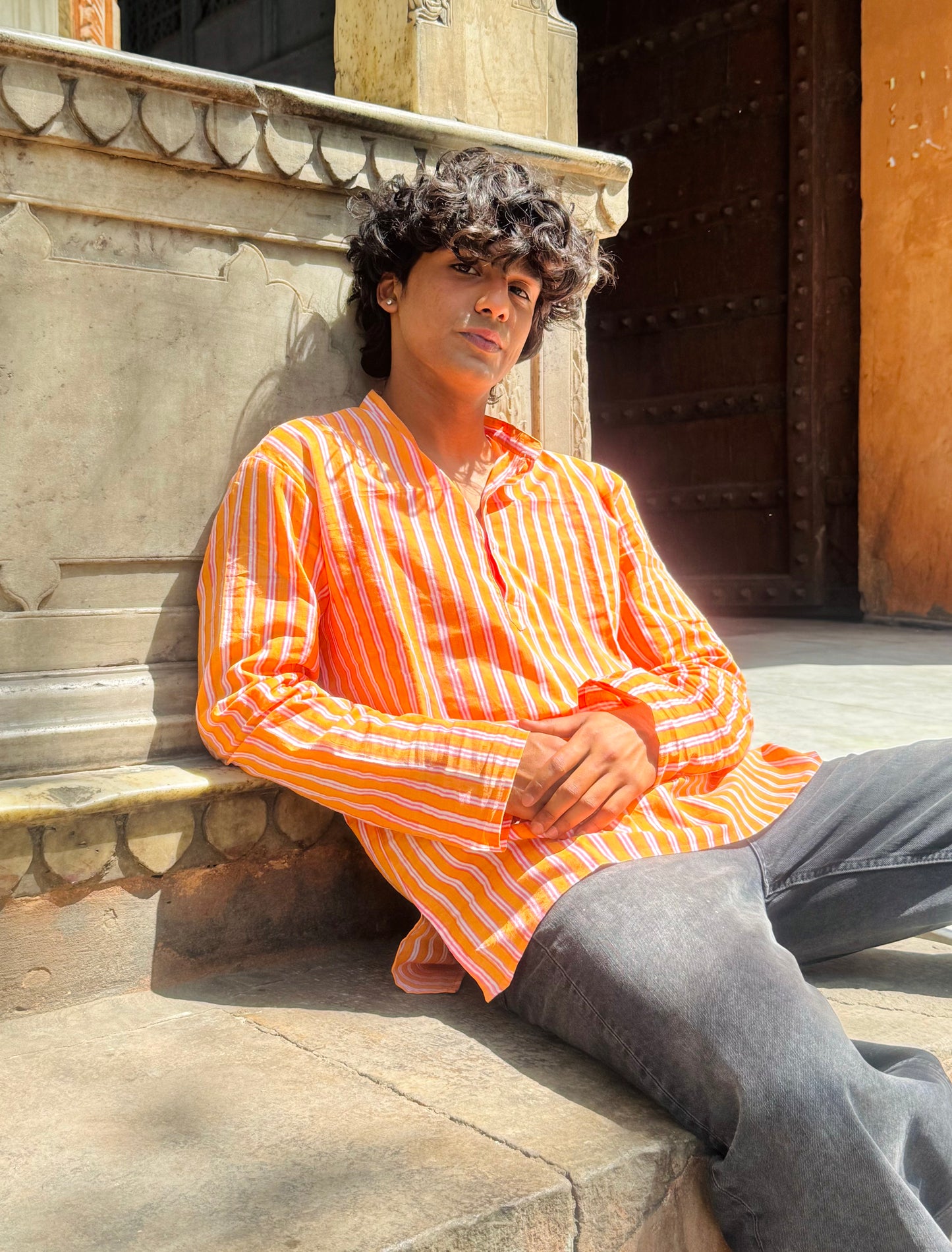 Person wearing an orange and white striped shirt sitting against a stone wall.