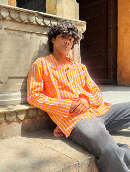 Person wearing an orange and white striped shirt sitting against a stone wall.
