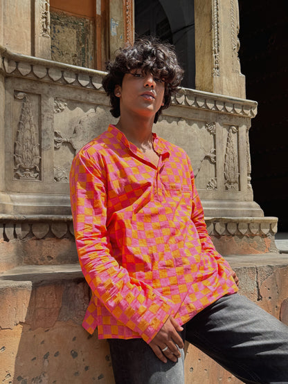 Person wearing a pink and orange patterned shirt sitting against an ornate wall.