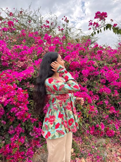 Woman in a floral dress standing among pink flowers with a cloudy sky.